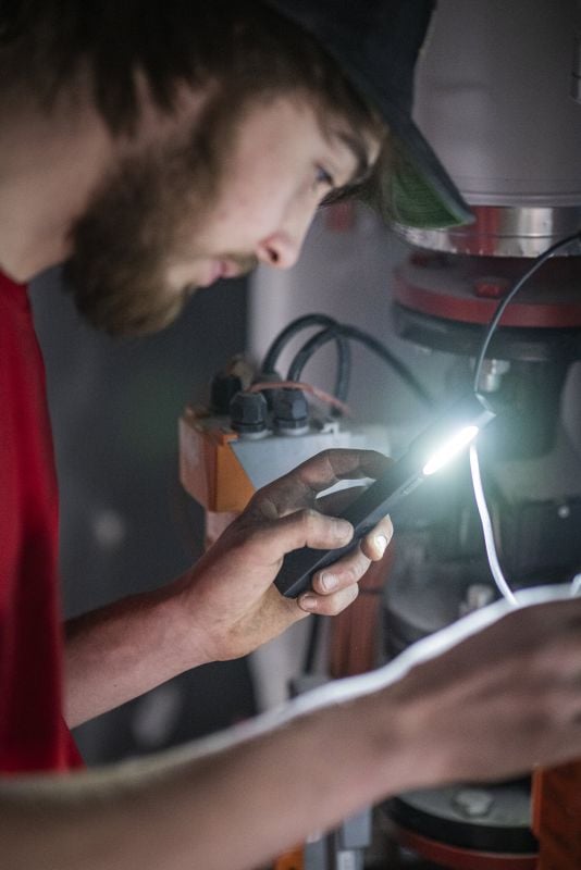 Handwerker leuchtet mit der LEDLENSER W2R Work in eine Maschine – Arbeitsleuchte als Werbeartikel