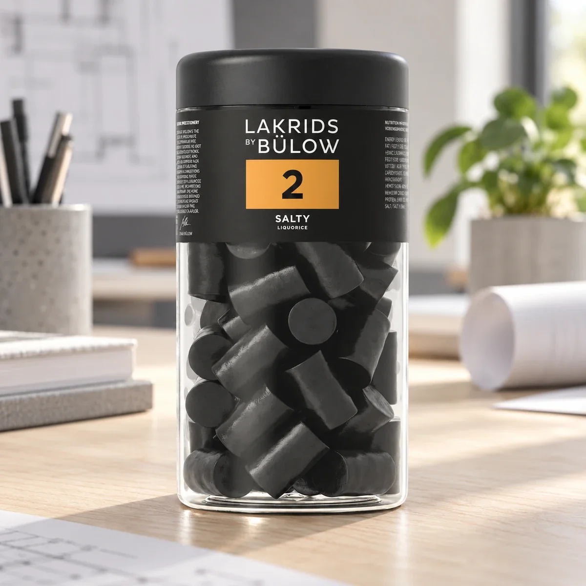 LAKRIDS BY BÜLOW Salty Lakritz im schwarzen Glas als hochwertiges Werbegeschenk auf dem Schreibtisch eines modernen Architekturbüros.