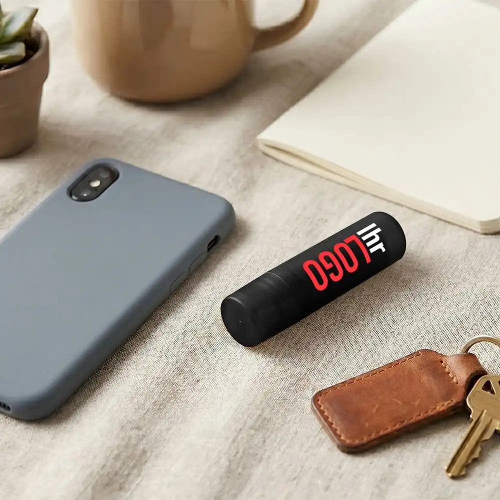 Schwarzer Deale Lippenpflegestift mit Logo neben Handy und Schlüsseln – praktischer Werbeartikel für Alltag und Branding