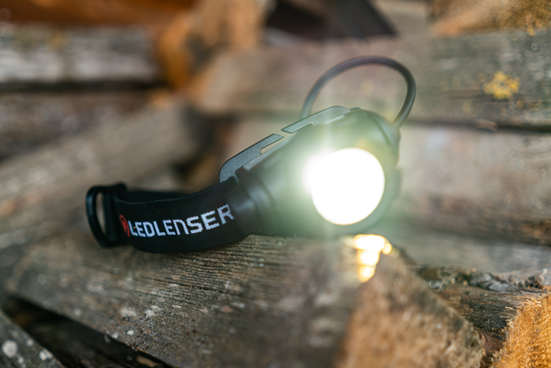Ledlenser Stirnlampe H7R Core LEDLENSER Stirnlampe H7R Core leuchtet auf einem Holzstapel – Akku-Stirnlampe zum Bedrucken