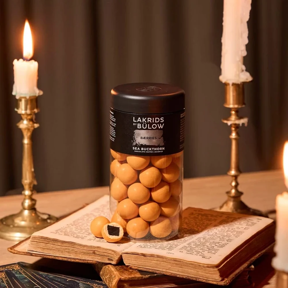 Lakrids by Bülow Sea Buckthorn Dose bei Kerzenlicht auf altem Buch – Halloween-Geschenk für Kunden