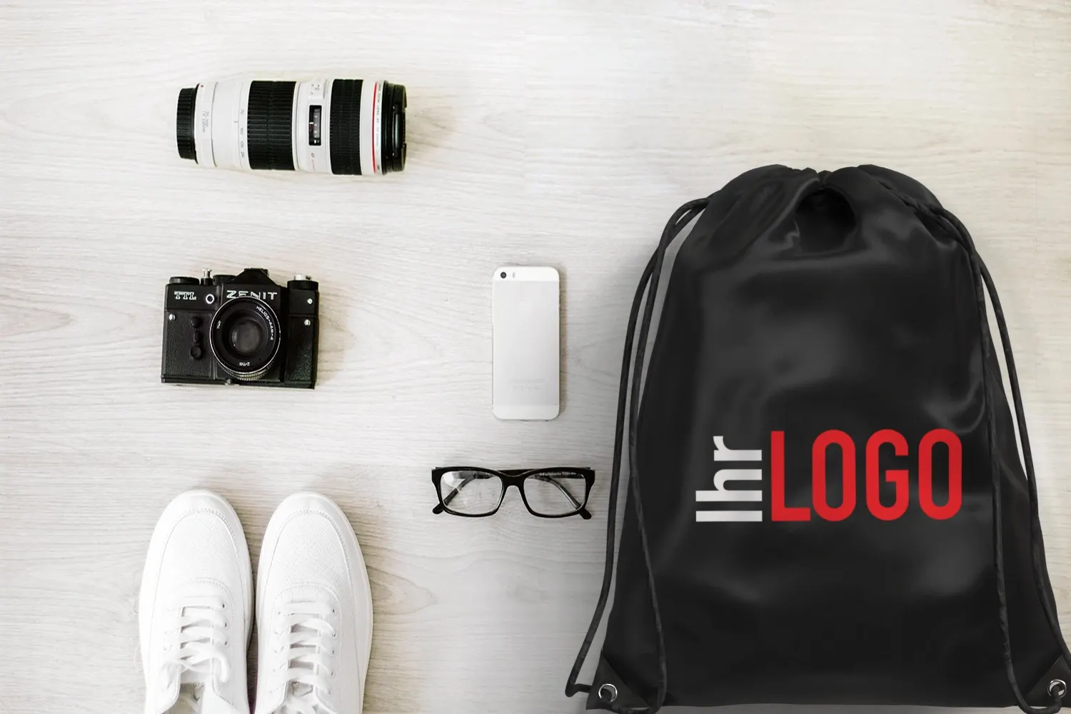 Evergreen Turnbeutel in Schwarz neben Brille, Sneakern und Kamera – praktischer Werbeartikel mit Logo